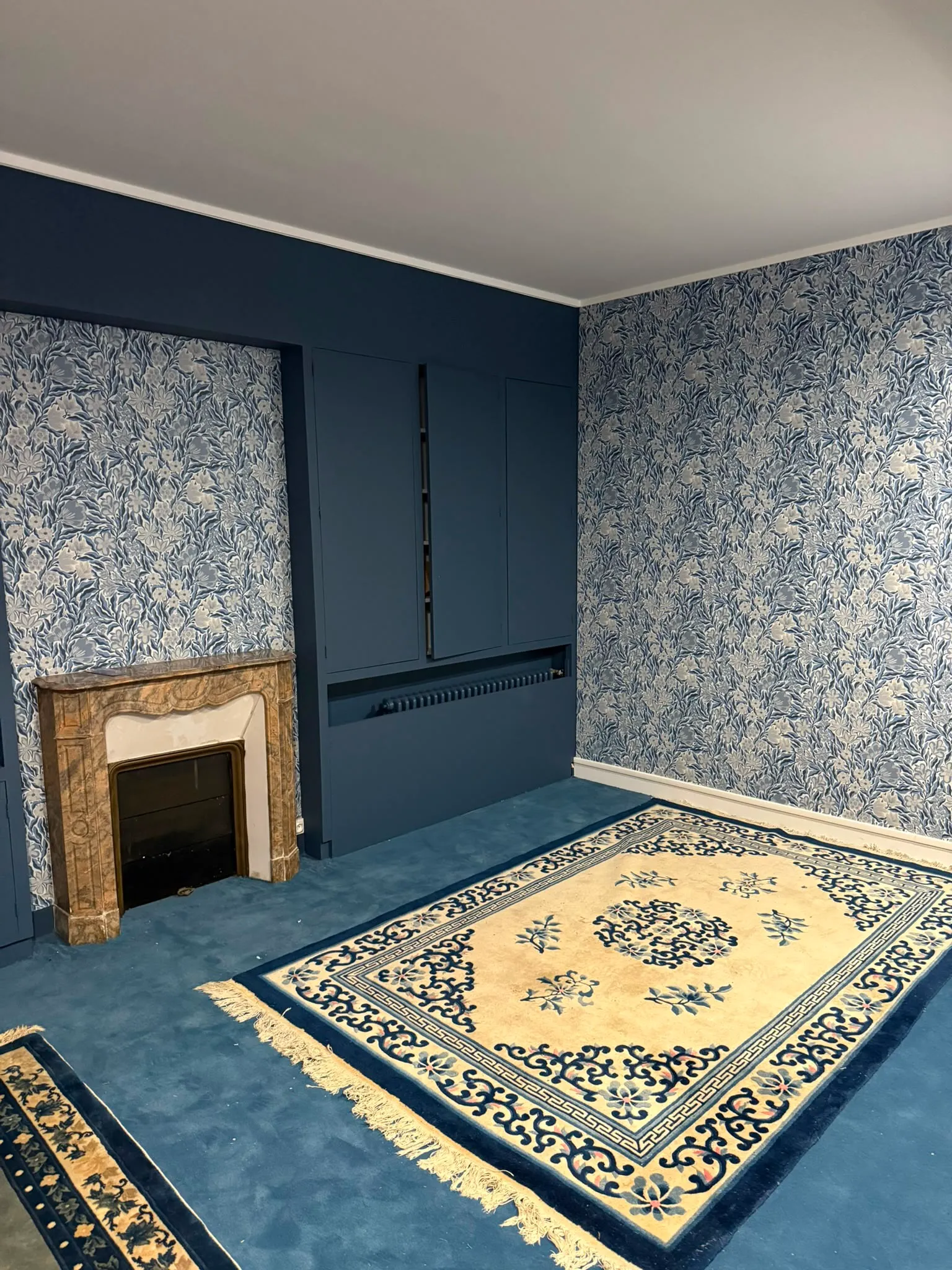 Chambre avec papier peint fleuri bleu et cheminée en marbre
