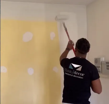 Peintre Bleau'décor appliquant une peinture jaune au rouleau sur un mur intérieur
